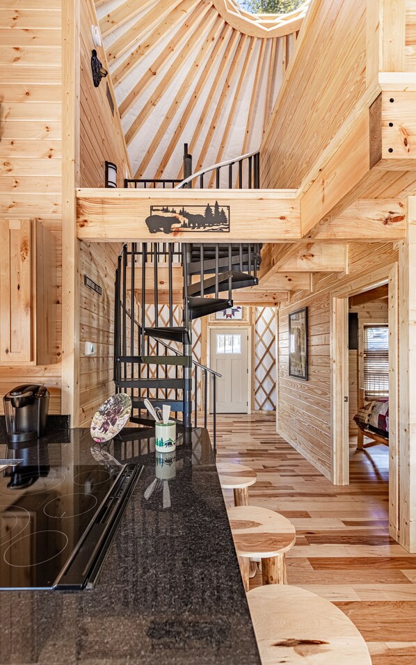 A modern wooden interior with a kitchen area featuring a black countertop, a spiral staircase, and a view of the outdoors. - Luxury Yurt Cozy & Fun 1br/1bth, experience it, Private Deck w Grill & HotTub (Pigeon Forge)