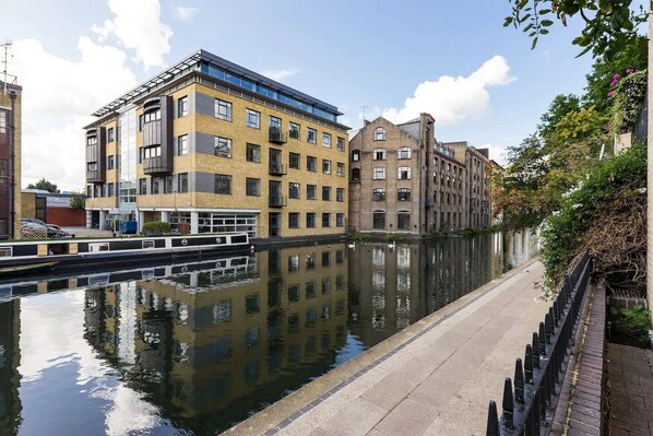 A canal with buildings on either side, including a modern building with large windows and a traditional brick building.
