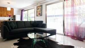 Una sala de estar moderna con un sofá modular negro, una mesa de centro de vidrio y un ventanal con cortinas translúcidas.