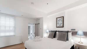 Ett modernt hotellrum med en stor säng, sängbord, en inramad tavla och utsikt över badrummet.