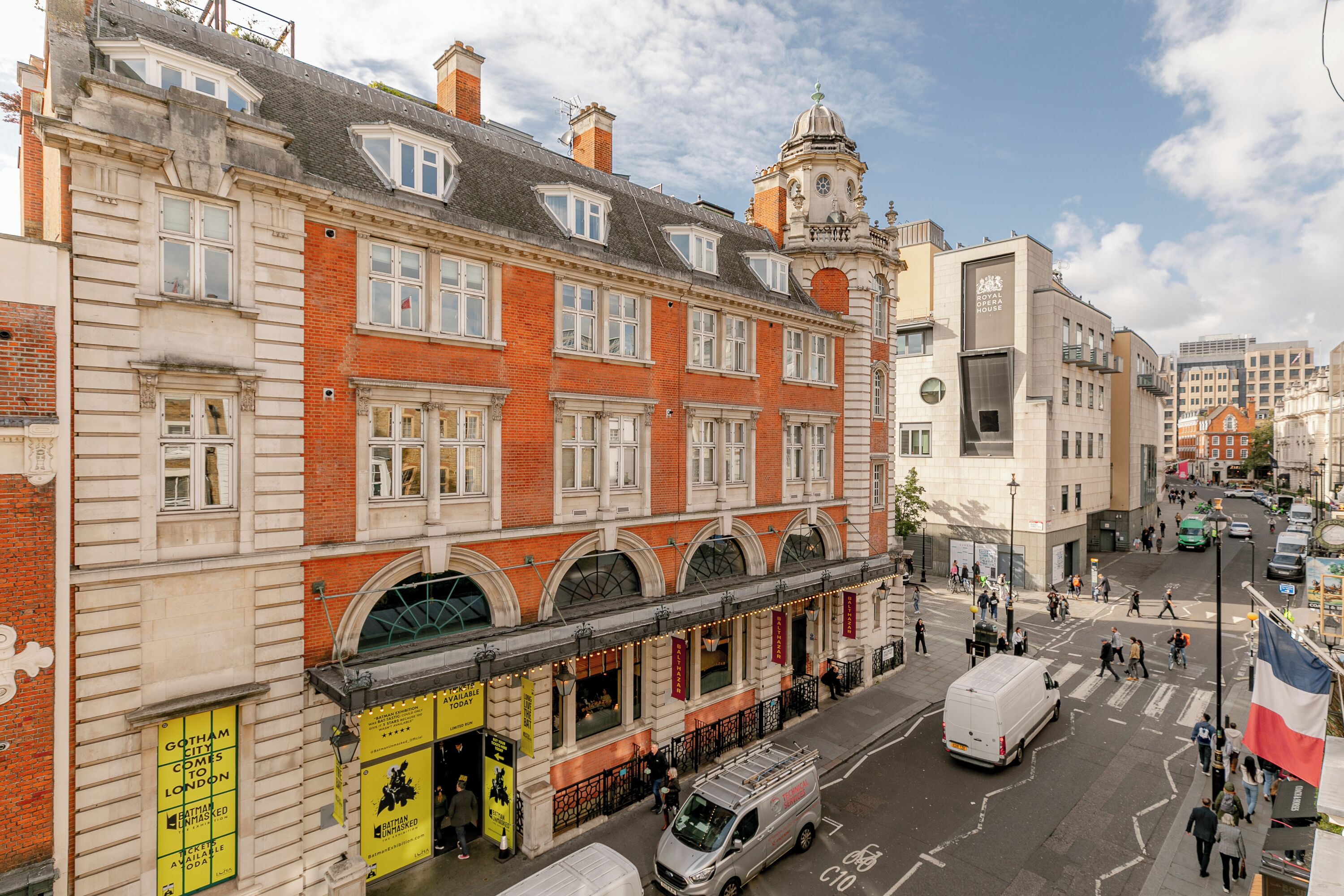 A historic building with a clock tower, large windows, and a street view with pedestrians and vehicles.
