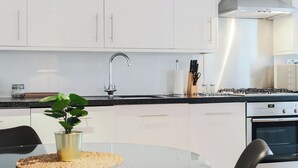 Ett modernt kök med vita skåp, en köksfläkt i rostfritt stål och ett matbord i glas med en svart stol.