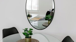 Ett modernt matområde med ett glasbord, svarta stolar, en krukväxt och en stor spegel på väggen.
