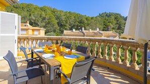 A terrace with a table set for breakfast, outdoor seating, and a view of a forested hill. - Villa Arata (Alcúdia)
