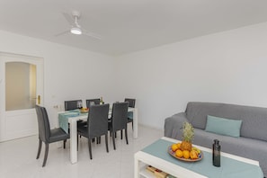 A modern living room with a dining area, a grey sofa, and a ceiling fan.