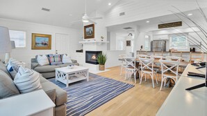 A spacious living room with a fireplace, a dining area with white chairs, and a kitchen with modern appliances. - Award-Winning Resort Amenities | Pelican Bay 38 (Isle of Palms)