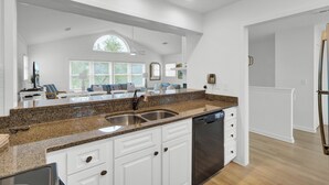 A modern kitchen with white cabinetry, granite countertops, a stainless steel sink, and a dishwasher. - Award-Winning Resort Amenities | Pelican Bay 38 (Isle of Palms)