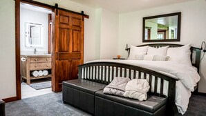 Ein Schlafzimmer mit einem großen Bett, einem Holzschrank, einer Bank mit Kissen, einem Spiegel und einem Badezimmer mit Toilette und Handtuchhalter.