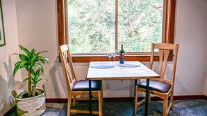 Ein Essbereich mit Tisch und vier Stühlen, einer Topfpflanze und einem Fenster mit Blick auf Bäume.