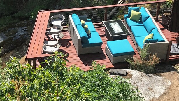 Eine Terrasse im Freien mit blauen Sitzkissen, einem Tisch mit Glasplatte und Korbstühlen.