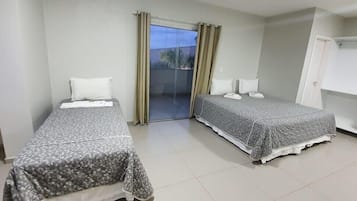 Quarto de hotel com duas camas de solteiro, porta de vidro deslizante para uma varanda e porta branca.