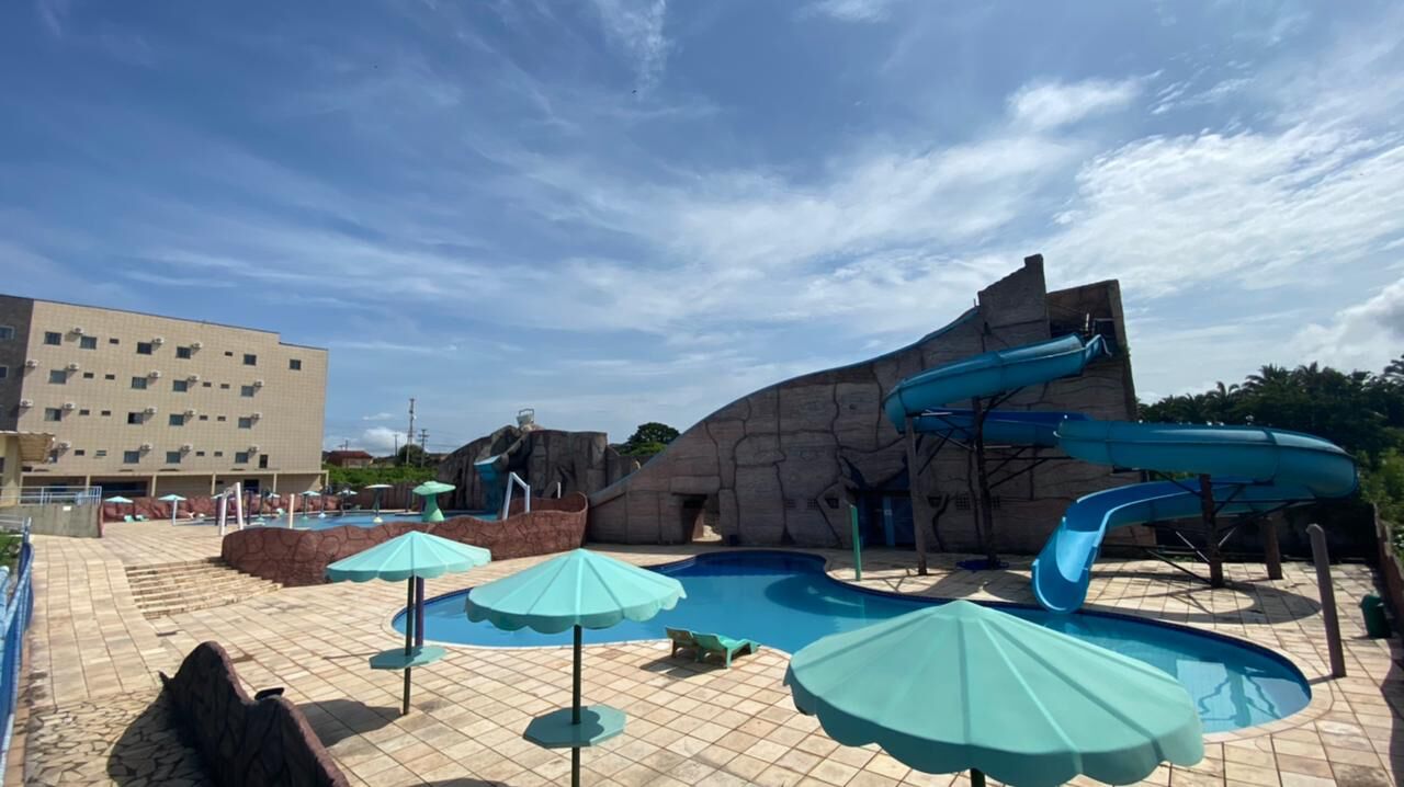 Uma área de piscina com várias escorregas, guarda-sóis e um edifício ao fundo.
