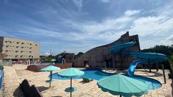 Uma área de piscina com várias escorregas, guarda-sóis e um edifício ao fundo.