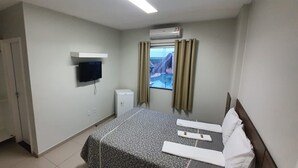 A hotel room with a bed, a TV mounted on the wall, a window with curtains, and a wardrobe.