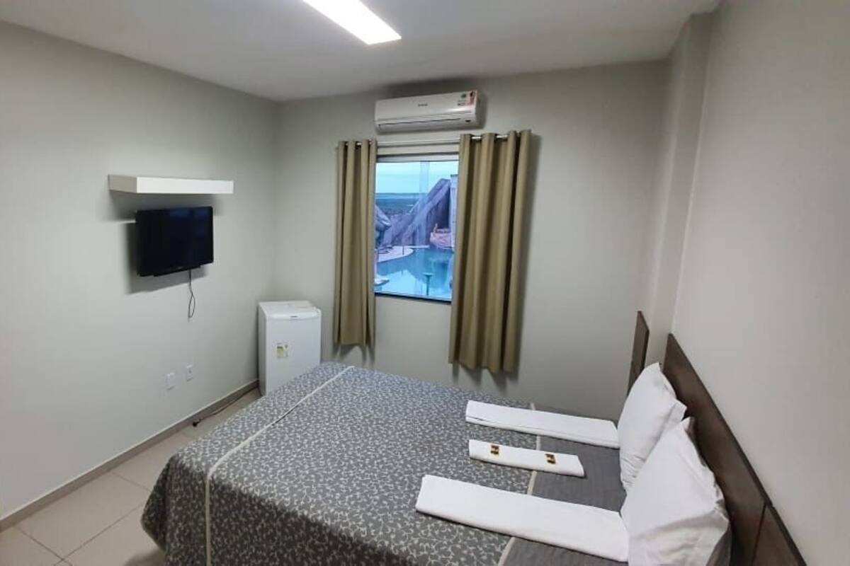 Hotellihuone, jossa on sänky, seinälle asennettu televisio, ikkuna verhoilla ja vaatekaappi.