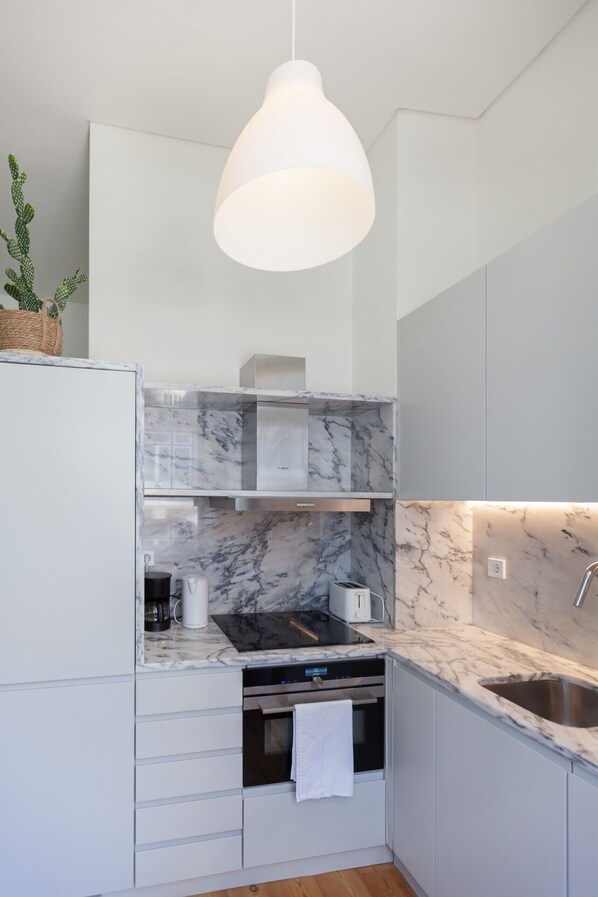 Una cocina moderna con armarios blancos, salpicadero de mármol y una lámpara colgante.
