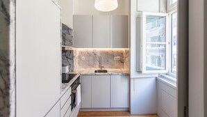 A modern kitchen with marble countertops, a built-in oven, and a window with a view of the city.