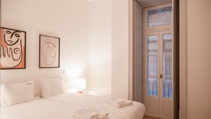 A hotel room with a large bed, two pillows, a nightstand with a lamp, and two abstract paintings on the wall.