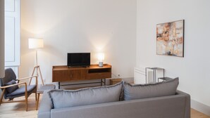 A modern living room with a grey sofa, a wooden TV stand, a floor lamp, and a painting on the wall.