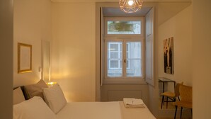 Een slaapkamer met een bed, een raam, een stoel en een muur met ingelijste foto's.