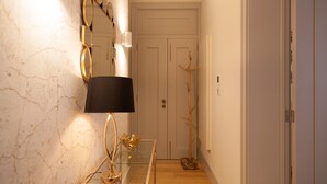 Een gang met een marmeren muur, een glazen tafel met een lamp, een spiegel en een houten deur.