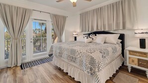Un dormitorio con cama, cortinas, ventilador de techo, mesita de noche y vistas al exterior.