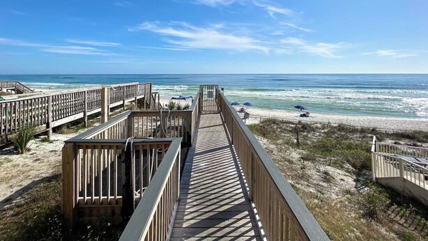 Una pasarela de madera que conduce a una playa con sombrillas y una vista despejada del océano.