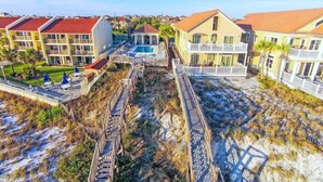 Un hotel frente al mar con varias construcciones, piscina y un paseo de madera que lleva a la playa.