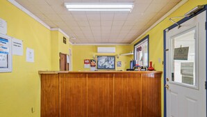 A reception area with a wooden counter, yellow walls, and a tiled floor. - OYO Hotel Luling TX Downtown I-10/US-90 (Luling)