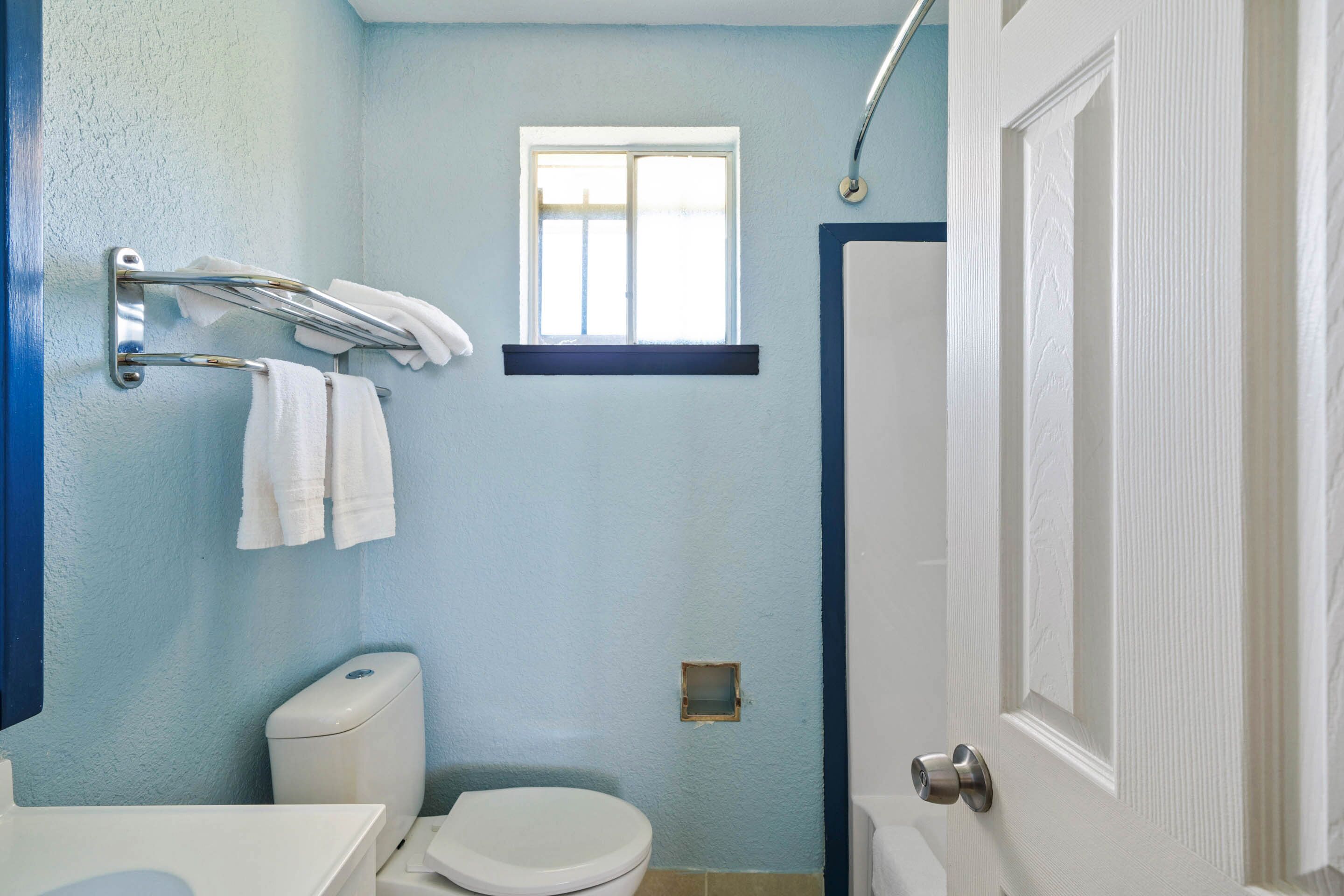 A bathroom with a toilet, a towel rack, a window, and a door.