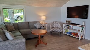 Ein Wohnzimmer mit Sofa, Sessel, Couchtisch, Fernseher und Bücherregal.