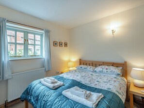 Ein Schlafzimmer mit Bett, Vorhängen am Fenster, Nachttisch mit Lampe und Wandleuchte.