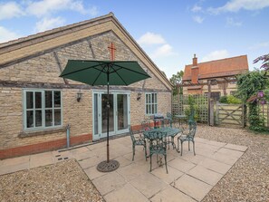 Un bâtiment en pierre avec un toit en tuiles, une clôture en bois et une terrasse aménagée avec du mobilier d’extérieur.