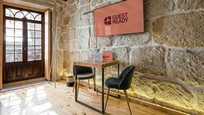 A stone-walled room with a wooden door, a table with chairs, and a 'GUEST READY' sign on the wall.