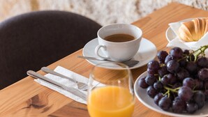 A wooden table with a white cup of coffee, a plate of grapes, a glass of orange juice, and a croissant.