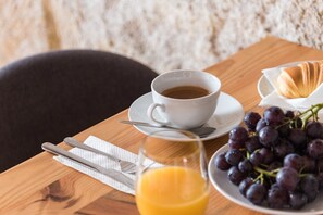 A breakfast setting with a cup of coffee, croissant, grapes, and orange juice on a wooden table.