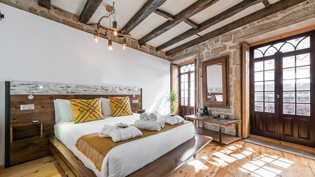 A bedroom with a wooden bed, a nightstand, a desk, and a large window with a view.