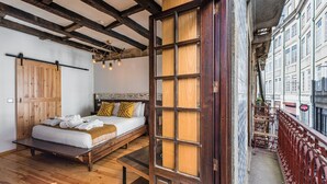 A room with a bed, wooden floor, and a large wooden door.