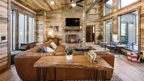 A spacious living area with a stone fireplace, leather sofas, and a wooden coffee table. - Modern and Luxury Cabin, 2 BR 2.5 Bath, Sleeps 9 max, 2 Pets Max with Pet Fee (Broken Bow)