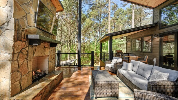 A stone fireplace, outdoor seating area, and large windows overlooking a forest. - Modern and Luxury Cabin, 2 BR 2.5 Bath, Sleeps 9 max, 2 Pets Max with Pet Fee (Broken Bow)