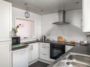 A modern kitchen with white cabinetry, a stainless steel sink, a built-in oven, and a clock on the wall.