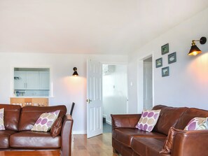 A living room with two brown leather sofas, a wooden coffee table, and a white door leading to a kitchen.