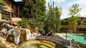 A pool area with a hot tub, surrounded by rocks and trees, and adjacent to a building with a staircase. - Aspenwood by iTrip Aspen Snowmass (Snowmass Village)