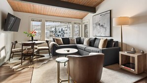 A modern living room with a wooden ceiling, a sectional sofa, a round coffee table, and a TV mounted on the wall. - Aspenwood by iTrip Aspen Snowmass (Snowmass Village)