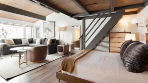 A modern bedroom with a wooden bed, a staircase, and a living area with a sofa and coffee table. - Aspenwood by iTrip Aspen Snowmass (Snowmass Village)