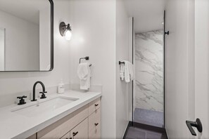 Un baño moderno con un espejo grande, un lavamanos con grifo y una cabina de ducha con paredes de vidrio.