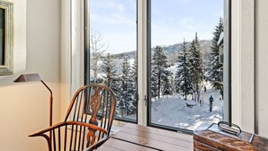 Une pièce dotée d’une grande porte-fenêtre coulissante qui donne sur un espace extérieur enneigé, avec des arbres et une personne qui se promène.