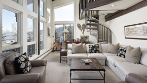 Un salon spacieux avec une grande fenêtre, un escalier en bois et un coin salon confortable.