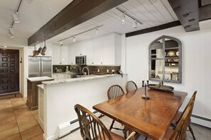 A kitchen with white cabinets, a stainless steel refrigerator, a microwave, and a sink with a faucet. There is a dining table with chairs and a mirror on the wall. - Interlude Condos by iTrip Aspen Snowmass (Snowmass Village)