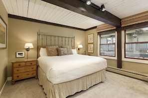 A bedroom with a large bed, wooden headboard, two bedside tables with lamps, a dresser, and a window with a view of the outside. - Interlude Condos by iTrip Aspen Snowmass (Snowmass Village)